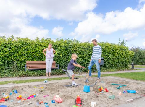 Vader en moeder kijken toe hoe kind in zandbak speelt